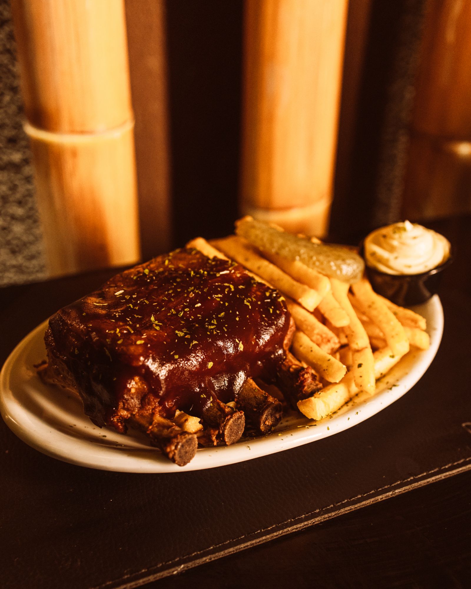Costela ao molho barbecue com batatas fritas, diante da parede de bambu