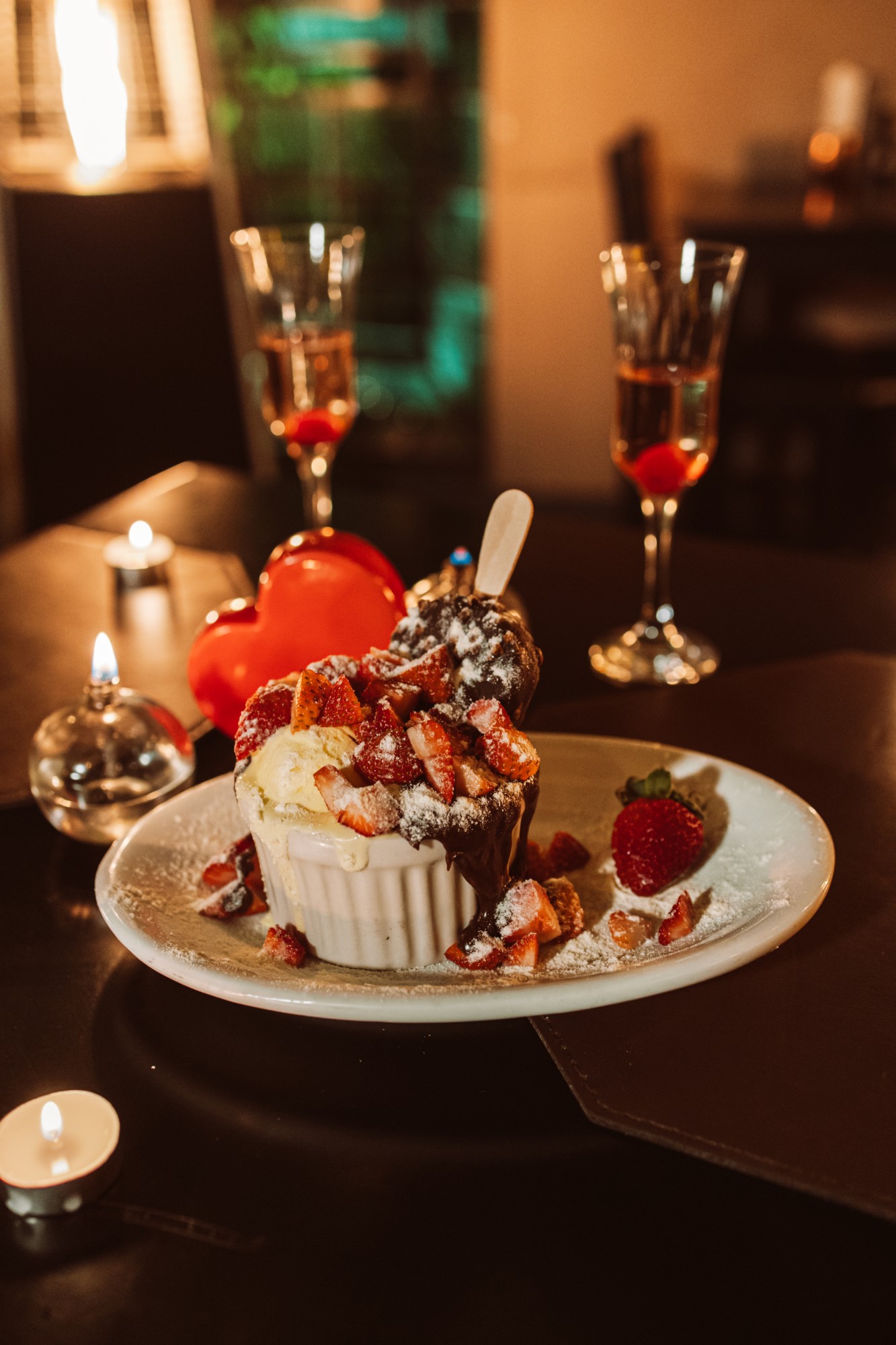 Sobremesa quente com sorvete, morangos e calda de chocolate, à luz de velas